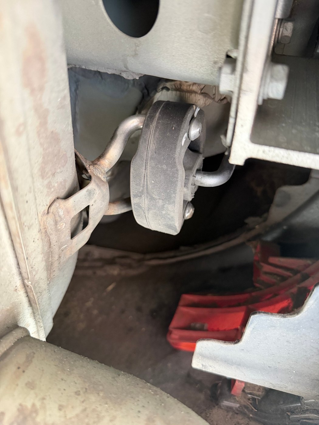 The forward rubber exhaust isolator in place between its body bracket and the exhaust hanger rod, before being cut
